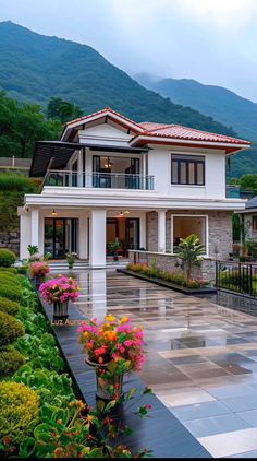 a large white house with flowers in the foreground and mountains in the back ground