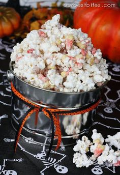 a metal bucket filled with white and pink popcorn on top of a table next to pumpkins