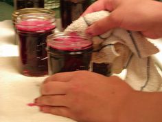 two hands are holding a towel over some jars with jams in them on a table