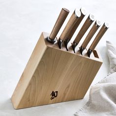 a wooden block with six knives in it on a white table cloth next to some napkins