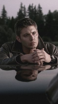 a man leaning on the hood of a car with his hands resting on his face