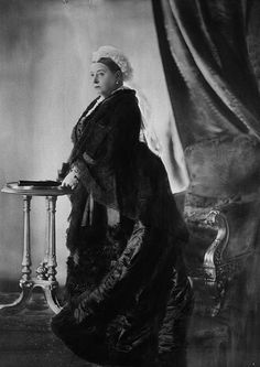 an old black and white photo of a woman in a fur coat sitting at a table