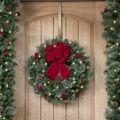 a christmas wreath with red bow hanging on a wooden door surrounded by evergreen and pine cones