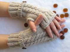 two hands wearing knitted mittens with beads scattered around them on a white surface