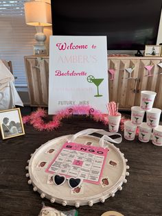 a wooden table topped with lots of cups and drinks next to a sign that says welcome to amber's bachelorette