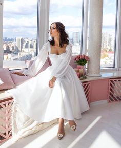 a woman in a white dress sitting on a window sill