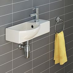 a white sink sitting next to a wall mounted faucet in a tiled bathroom