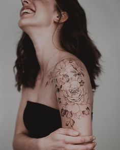 a woman with a flower tattoo on her arm and shoulder, smiling at the camera