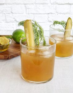 two glasses filled with drinks sitting on top of a wooden cutting board next to limes