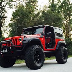 a red jeep is parked on the side of the road in front of some trees