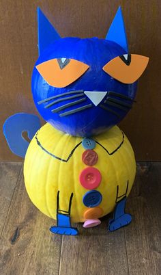 a blue cat sitting on top of a pumpkin with buttons in its mouth and eyes