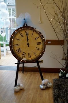 a large clock sitting on top of a wooden floor next to a vase filled with flowers