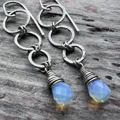 These long dangle earrings are handmade from sterling silver and Opalite. The small Opalite teardrops are wrapped in sterling silver. Above the teardops are a set of rings which I have formed, soldered, and hammered by hand. The earrings dangle from handmade sterling silver earwires. The silver has been oxidized and polished to create an antique patina finish.Be sure to see all photos and video for size and color reference.Opalite: About 5x7mmTotal Earring Length: Just over 2 inchesTotal Earring Sterling Silver Teardrop Pendant Jewelry With Ear Wire, Sterling Silver Teardrop Pendant With Ear Wire, Unique Handmade Sterling Silver Teardrop Earrings, Silver Teardrop Jewelry With Hand-wrapped Detail, Hand Wrapped Sterling Silver Dangle Jewelry, Hand Wrapped Teardrop Silver Jewelry, Hand Wrapped Silver Teardrop Jewelry, Sterling Silver Wire Wrapped Long Drop Jewelry, Wire Wrapped Long Drop Sterling Silver Jewelry