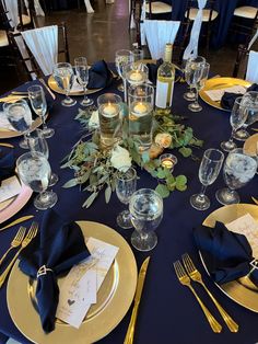 the table is set with blue linens and gold plates, silverware, and candles