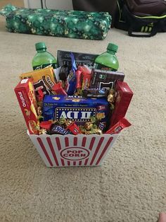 a popcorn box filled with snacks and drinks on the floor in front of a couch