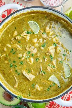 a bowl filled with green soup and garnished with limes on the side