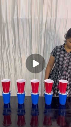 a woman standing in front of a table filled with red and blue cups on top of it