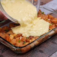 a person pouring sauce over food in a glass dish on top of a wooden table