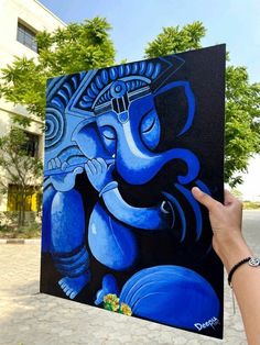 a person holding up a painting with an elephant on it's face in front of a building