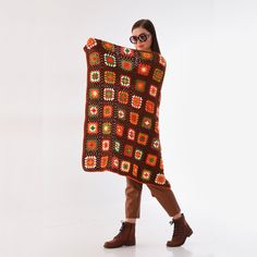 a woman is holding up a crocheted blanket