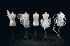 four mannequins with different types of dresses on display in front of a black background