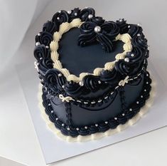 a heart shaped cake with black frosting and pearls on the top is sitting on a white surface