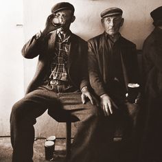 two men sitting next to each other on a bench with beer in their hands and one man holding a camera up to his face