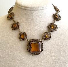 Gorgeous Antique Art Deco Facetted Czech Amber Glass Necklace. Antique gold tone filigree metal frames each amber color glass stone set in crenelated bezel. Hidden slide clasp behind upper corner center piece. Measurements: 15" long Center pendant  1 1/4" Surrounding squares 3/4" Luxury Antique Amber Necklace, Antique Jeweled Jewelry For Formal Occasions, Antique Formal Jewelry, Ornate Jeweled Necklaces For Formal Occasions, Vintage Metal Jewelry With Intricate Design, Antique Gold Evening Jewelry, Antique Gold Jewelry For Evening, Antique Formal Jewelry With Cabochon, Antique Brass Jewelry For Evening