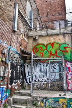 an alleyway with graffiti on the walls and steps leading up to some stairs in front of a fence