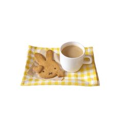 a cup of coffee next to a cookie on a yellow and white checkered cloth