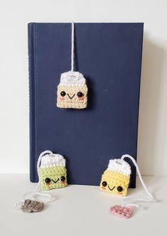 two small crocheted items are hanging on a book with twine strings attached to them