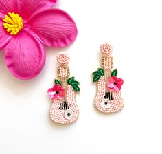 the pink flower is next to two earrings with flowers on them and one has green leaves