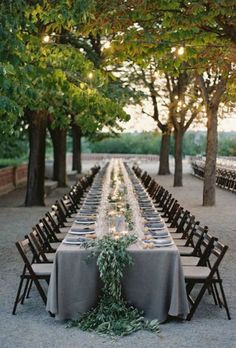 a long table is set up in the middle of an outdoor setting with candles and greenery