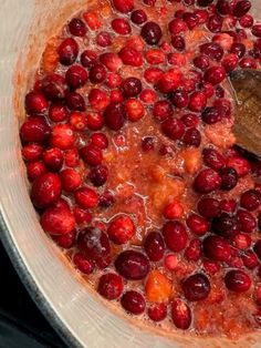 cranberry sauce being stirred in a pot with a wooden spoon on the side