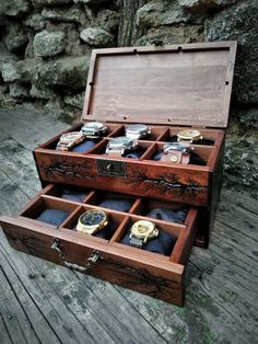 an open wooden box with watches inside on a wood floor next to a rock wall