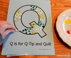 a child's hand is writing the letter q on a piece of paper next to a plate with jelly beans