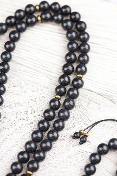 A DharmaShop exclusive 108 bead mala made from powerful, unique materials with a story! Features 108 shungite beads and a handcrafted vintage Buddha protection amulet from Thailand. Shungite is known as one of the most powerful mineral healers. It has the ability to protect and purify. Black stones like shungite are known to offer protection to the wearer, provide stability, and ground the Root Chakra. Over a decade ago, during a trade with a Tibetan artifacts collector, we received a small bag Spiritual Black Natural Stone Beads, Traditional Black Mala With 108 Beads, Black Gemstone Beads Mala For Healing, Black Natural Stones Beads For Healing, Handmade Black Mala For Meditation, Handmade Black Mala As Gift, Traditional Black Mala With 8mm Beads, Traditional Black Beads With Natural Stones, Black Natural Stones Beads For Meditation