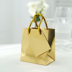 "Quantity: 12 Gift Bags Material: Paper Color: Metallic Gold Bag Height: 4.75\" Bag Width: 2.75\" Bag Length: 4\" Handle Length: 5\" Tag Size: 2.4\"L x 2.75\"W Features: Premium paper, lightweight, durable, reusable Sturdy metallic rope handles ensure comfortable and stylish carry Metallic Gold Foil Paper Gift Bags A stunning and sophisticated way to package your gifts or party favors, these Shiny Metallic Gold Paper Gift Bags feature a glossy metallic gold finish that is sure to impress. These Gold Party Favors, Wedding Guest Bags, Small Paper Bags, Small Party, Gold Foil Paper, Merchandise Bags, Gold Bag, Foil Paper, Paper Color