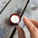 a person holding a candle in their left hand on a wooden table next to two empty wine glasses