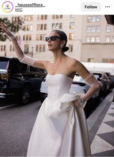 a woman in a white dress is standing on the street with her arms outstretched and wearing sunglasses