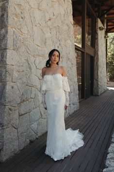 a woman in a white wedding dress standing on a wooden deck next to a stone building