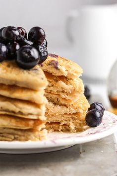 a stack of pancakes with blueberries and syrup on the side sitting on a plate