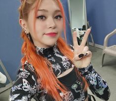 a woman with orange hair is making the peace sign