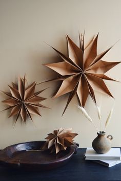 three paper stars are hanging on the wall above a bowl and vase with flowers in it