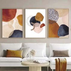 three paintings hanging on the wall in a living room with white furniture and large pillows