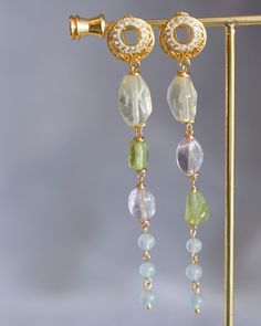 Crafted from the finest materials, these elegant earrings are a charming combination of 14K gold filled wires and a selection of luxurious gemstones, including Lemon Quartz, Amethyst, Peridot, and Aquamarine. Suspended from a pair of cubic ear hoops, they offer a unique accent to your everyday wardrobe or a thoughtful gift for someone special. Images cannot capture their beauty - you must see them in person to appreciate their grandeur. Follow me on Instagram: @cubic_jewels Dainty Gold Earrings With Gemstone Accents, Gold Dangle Gemstone Linear Earrings, Elegant Gold Linear Earrings With Natural Stones, Gold Dangle Crystal Earrings With Gemstone Accents, Gold Long Drop Jewelry With Gemstone Accents, Gold Plated Earrings With Gemstone Accents, Gold-plated Earrings With Gemstone Accents, 14k Gold-filled Yellow Gold Earrings With Natural Stones, Elegant 14k Gold Filled Earrings With Natural Stones