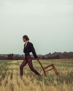 a woman in tights carrying a chair across a field