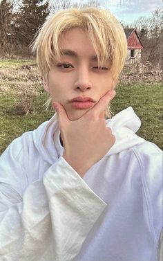 a young man with blonde hair wearing a white shirt and looking at the camera while standing in a field