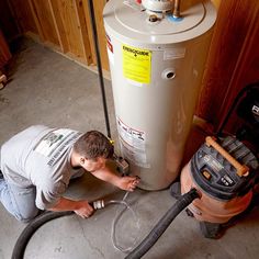 a man is working on a water heater in the garage with a hose connected to it