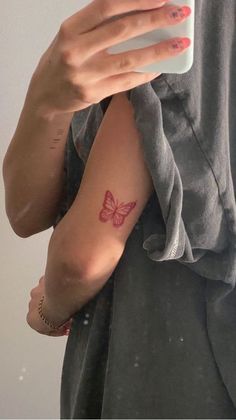 a woman with a butterfly tattoo on her arm holding a cell phone and taking a selfie